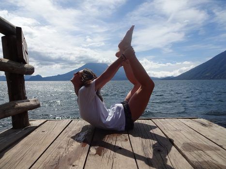 Bow pose, holding the ankles, chest lifted, on a dock.