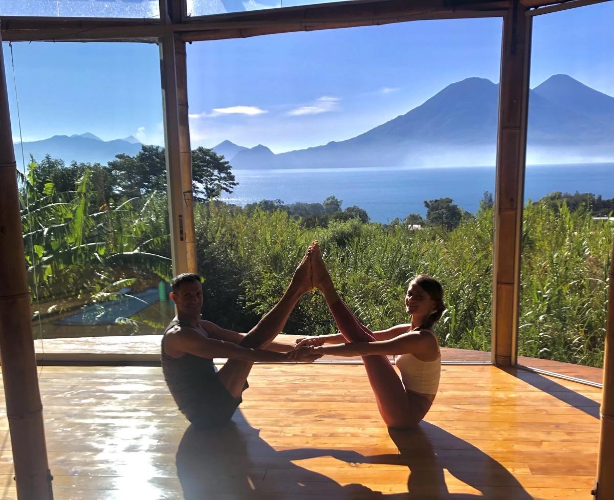 Doron practicing a partner pose with a student, lake behind them