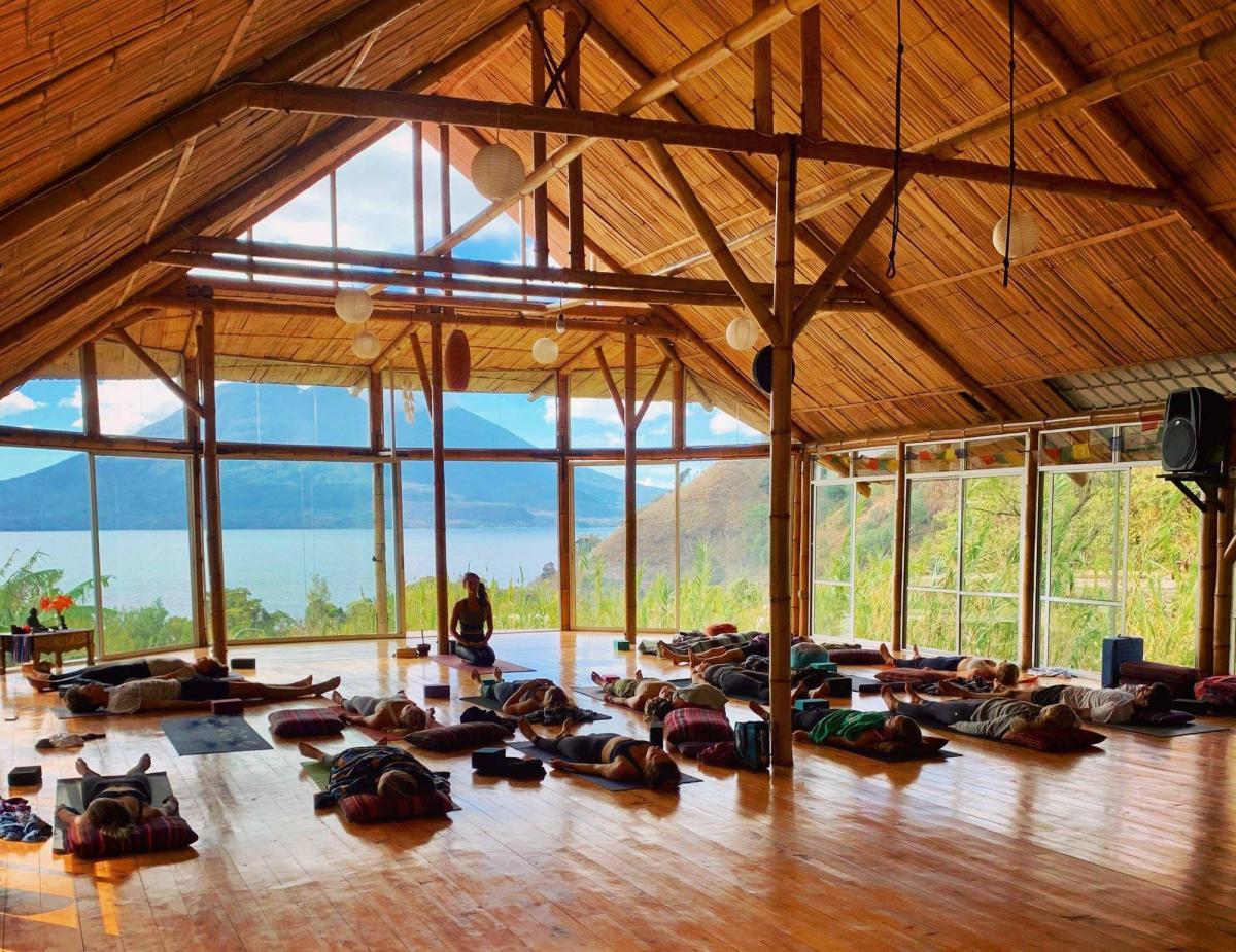 A large yoga class seated in a wooden hall.