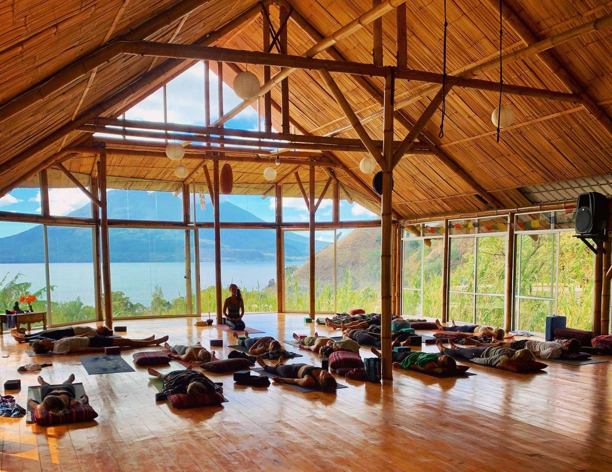 A large yoga class seated in a wooden hall.