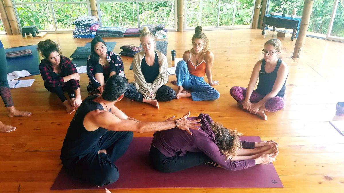 A teacher assisting a seated forward fold.