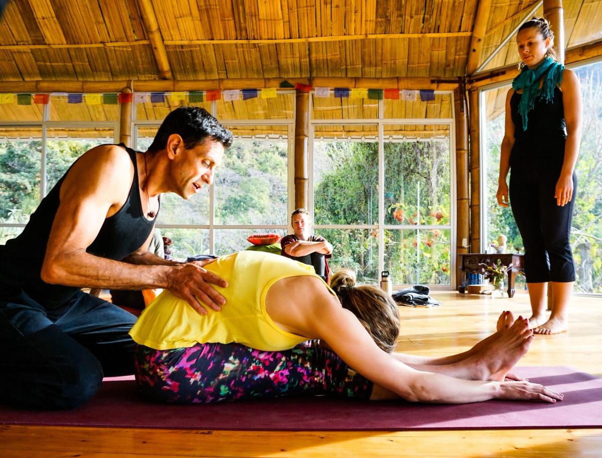Doron rests a hand on a student's back during a seated forward fold.