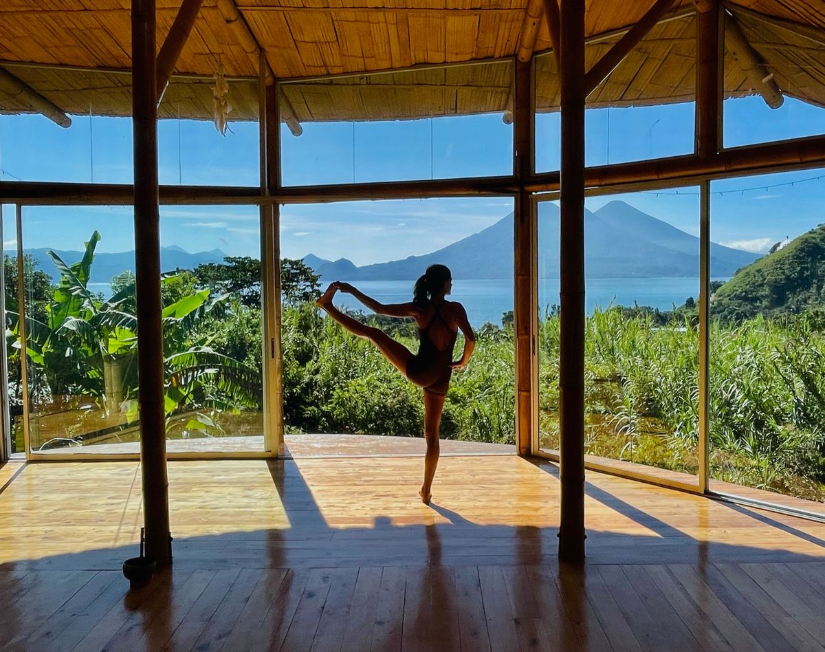 Dancer pose, holding the back foot, in a shala open to the lake.