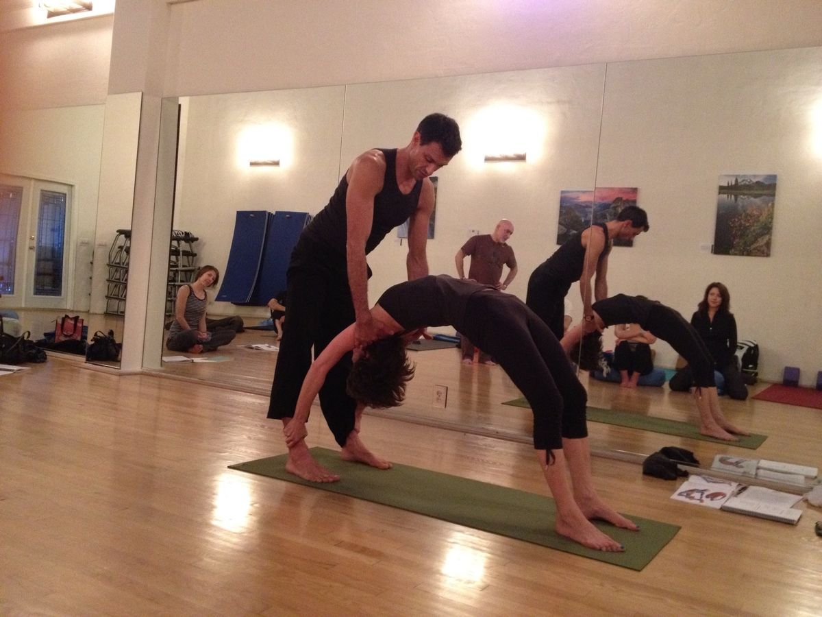 A teacher assisting a student in wheel pose.
