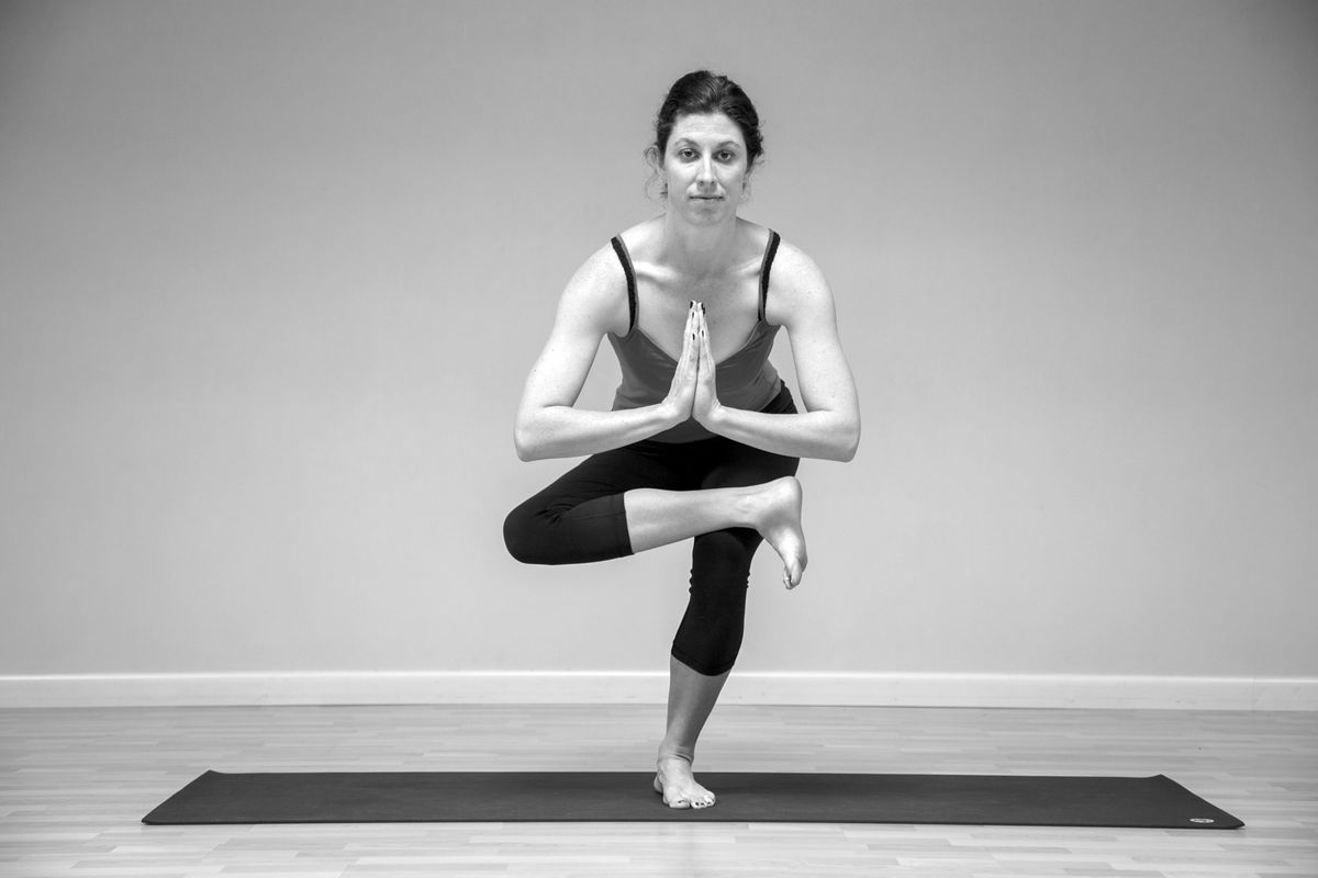 Standing with one ankle crossed over the opposite knee, the cappuccino pose, a hip opener that prepares for eka pada galavasana