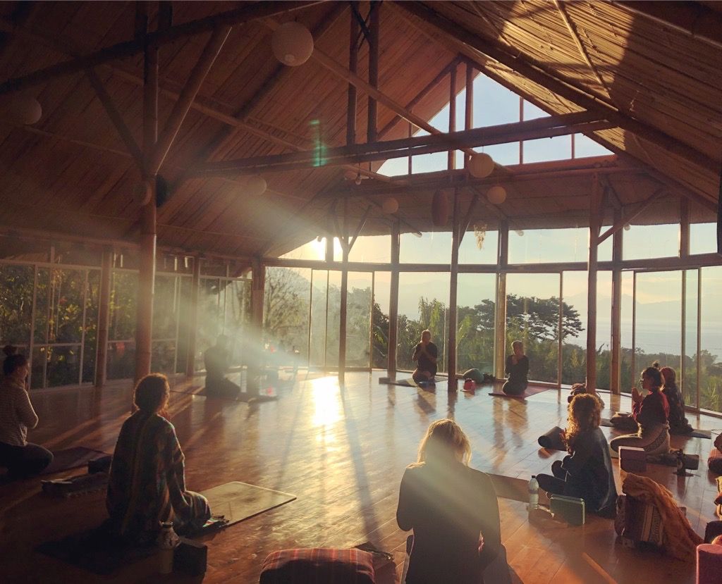 A morning class seated in a wooden shala as the sun comes in.