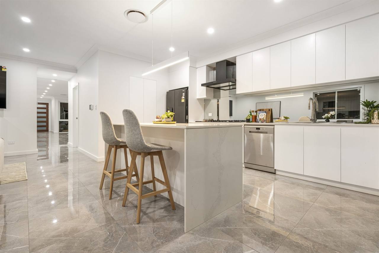 Wide view of Sandstone Residence kitchen island with bar stools and marble-look floor