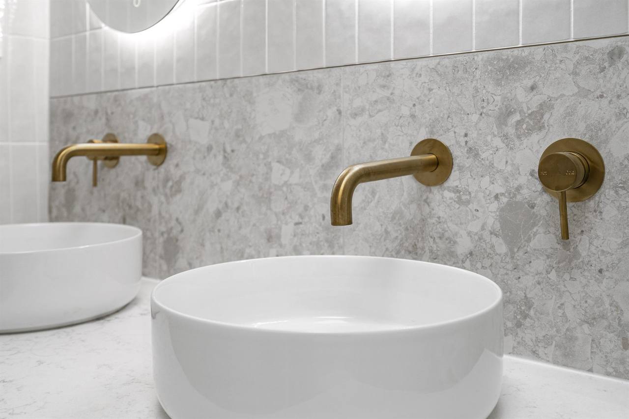 Twin basins with brushed brass tapware on grey terrazzo splashback