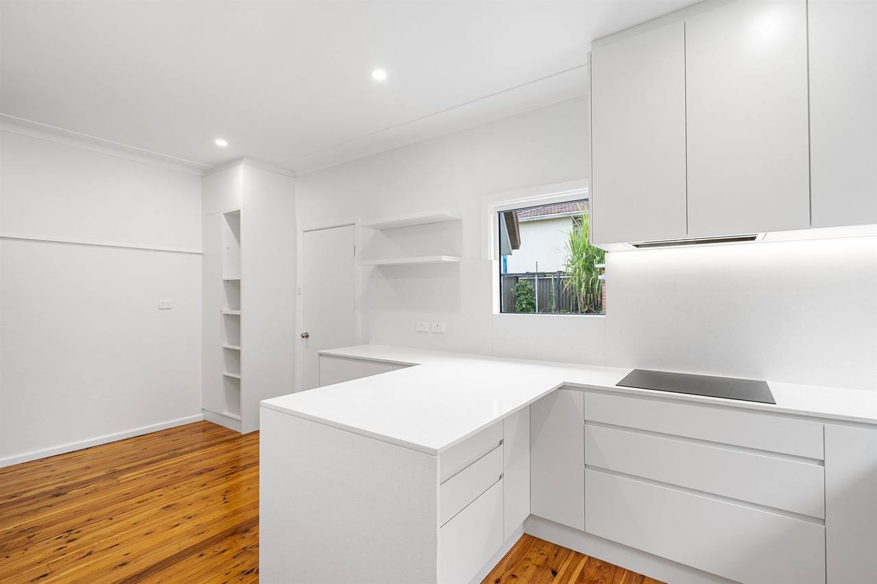 Compact white kitchen with stainless dishwasher and stone benchtop — Berala