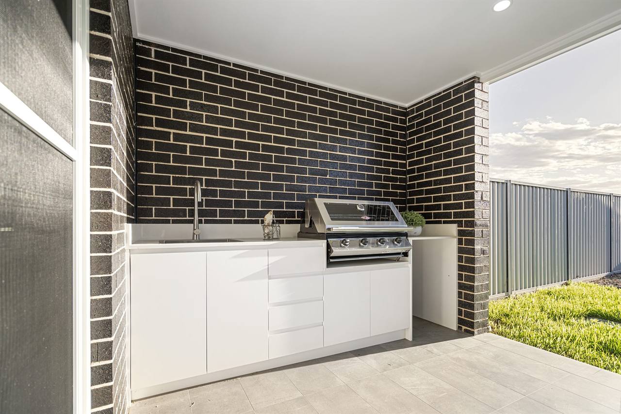 Outdoor BBQ wing wrapped in dark feature brick with white cabinetry — Sandstone Residence