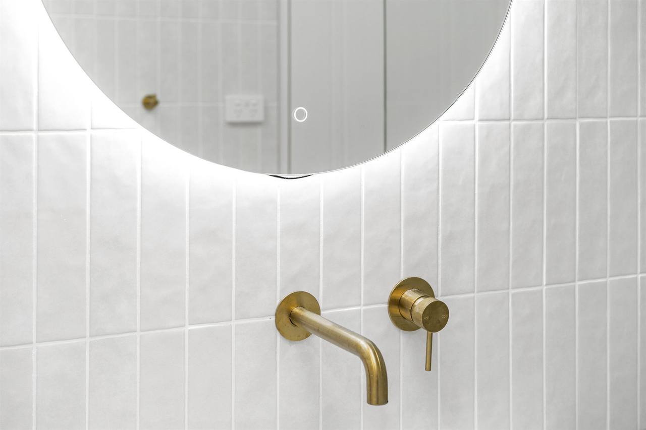 Round LED back-lit mirror above brass tapware and round white basin