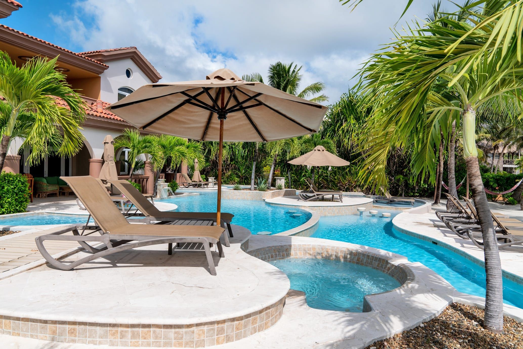 Resort pool and hot tub with a stucco building and palm trees behind