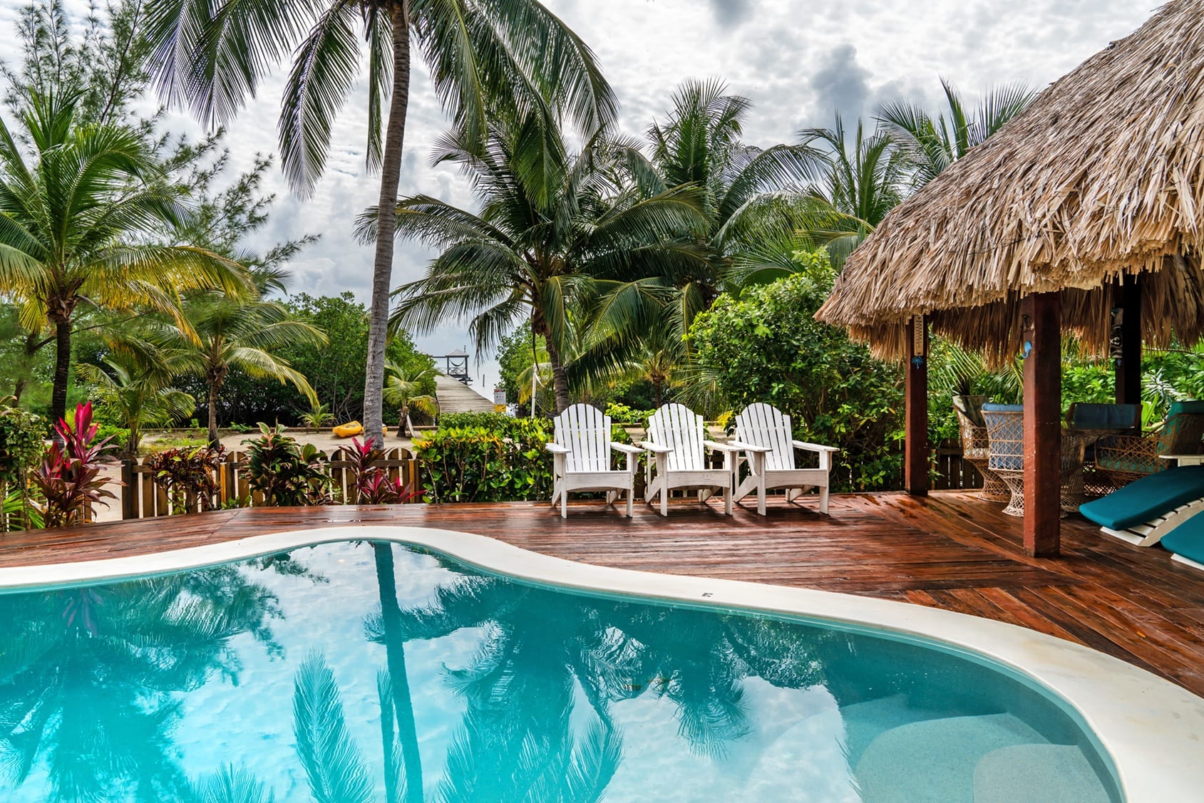 Swimming pool with a thatched palapa and white Adirondack chairs