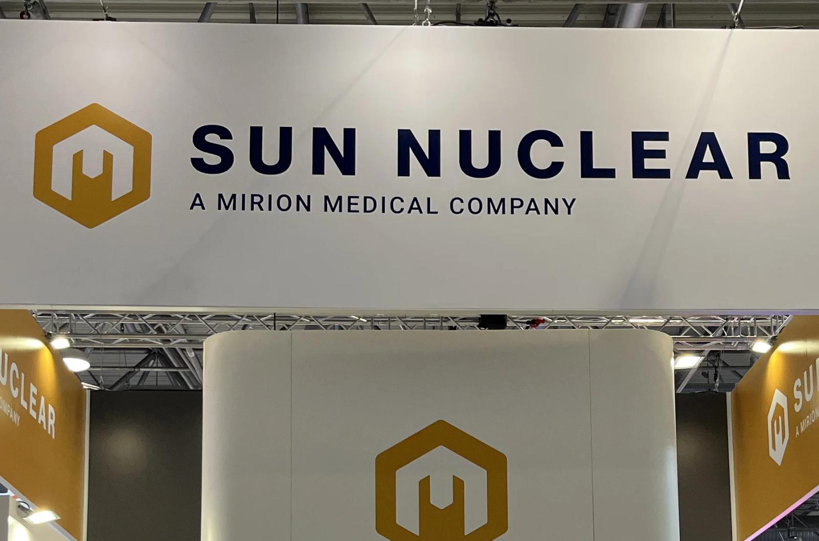 Sun Nuclear exhibition stand with a white overhead sign reading Sun Nuclear, A Mirion Medical Company, gold hexagon logos and gold side canopies