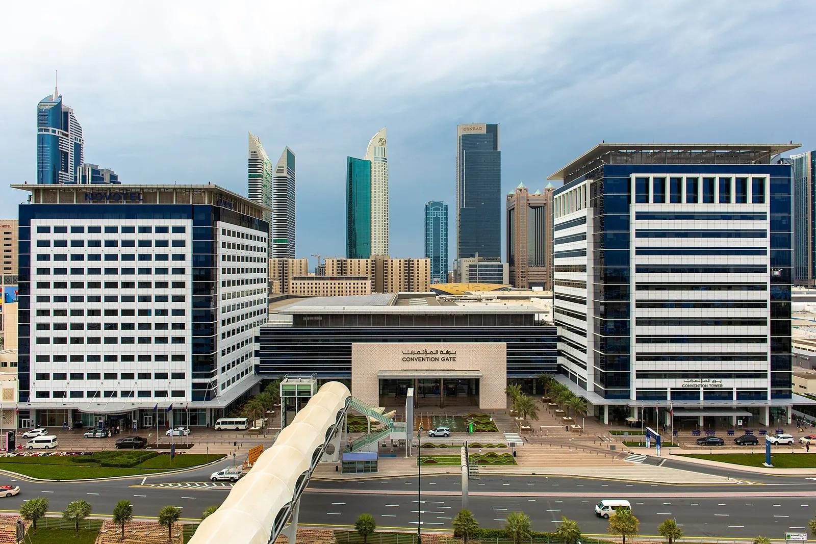 Convention Gate entrance building at Dubai World Trade Centre between two blue and white towers, with skyscrapers behind