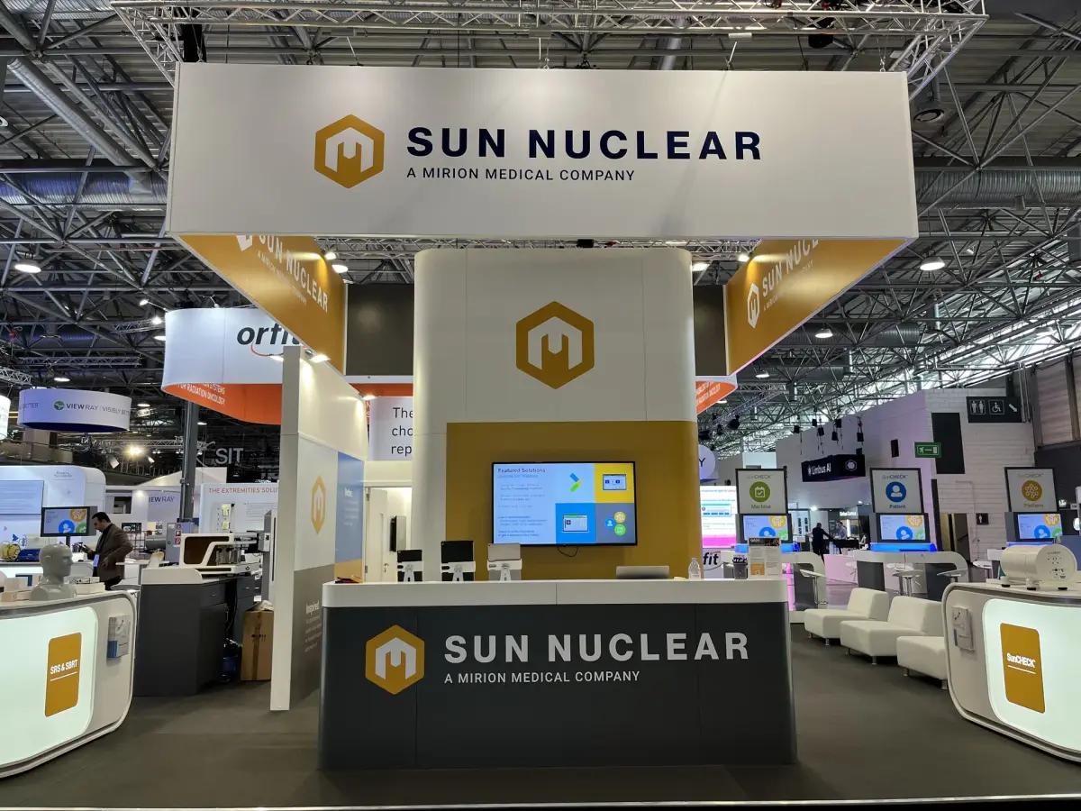Custom exhibition stand with a suspended overhead banner, reception counter, product display units and visitor seating, built by Orchestra Media