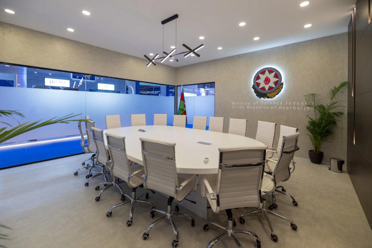 Private delegation meeting room inside a national defence pavilion with the national flag and ministry crest