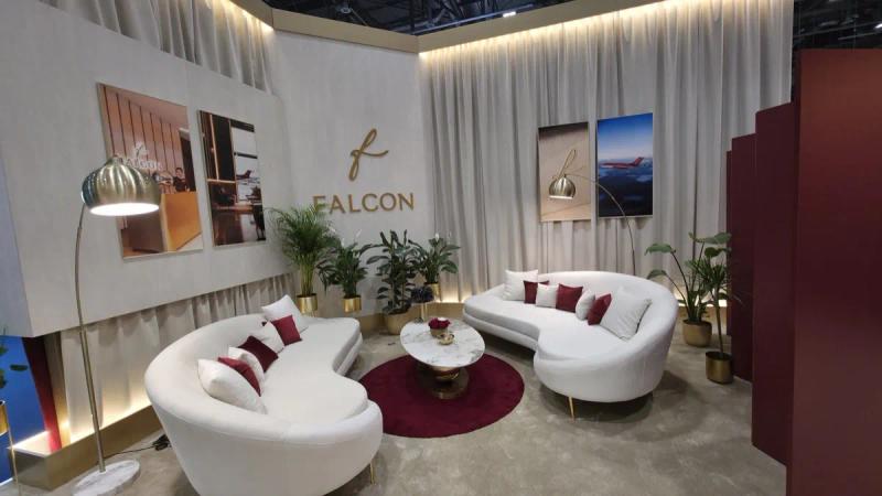 Lounge area of a Falcon Aviation exhibition stand, with white curved sofas, burgundy cushions and aircraft artwork