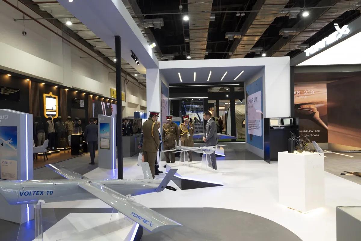 Technology exhibition stand with open product display plinths and visitors in discussion on the show floor