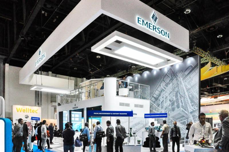 Double-deck technology exhibition stand with overhead branding on a busy UAE trade show floor