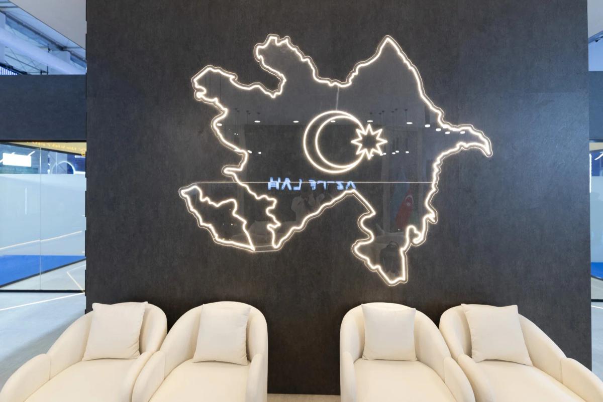 Neon outline map of Azerbaijan with a crescent and star on a dark wall, above four cream armchairs