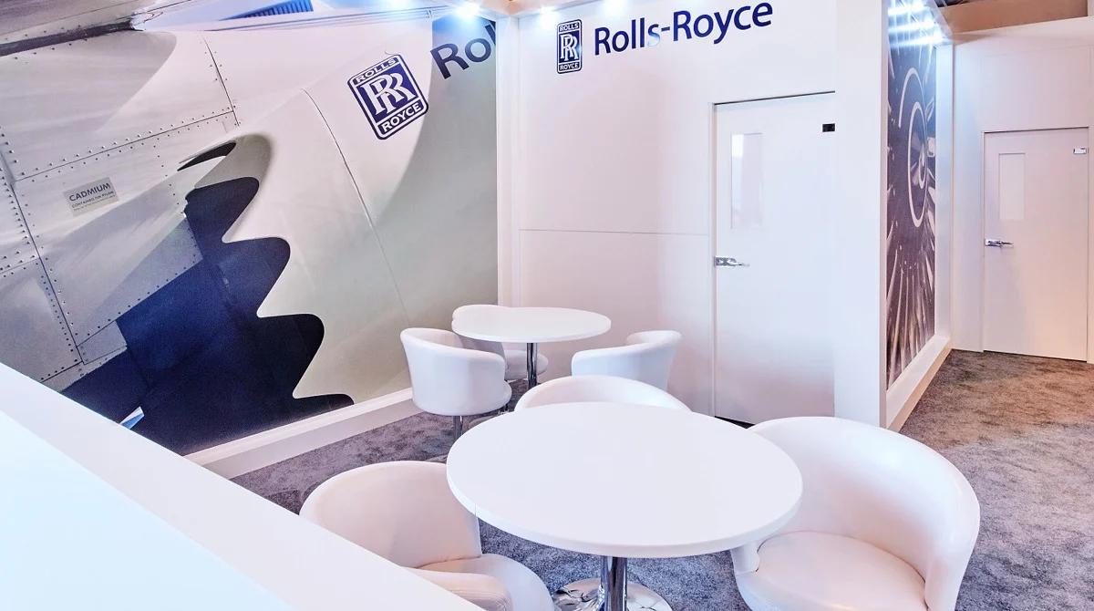 Rolls-Royce exhibition stand meeting area with white tub chairs, round tables and a large engine nacelle graphic