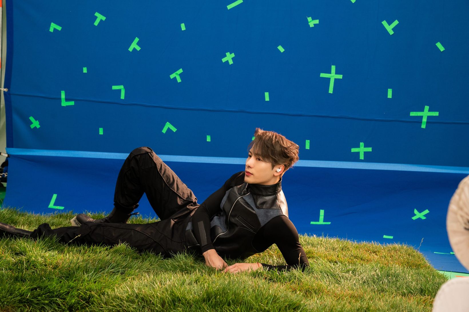 Jackson Wang lying on turf in front of a blue screen on set