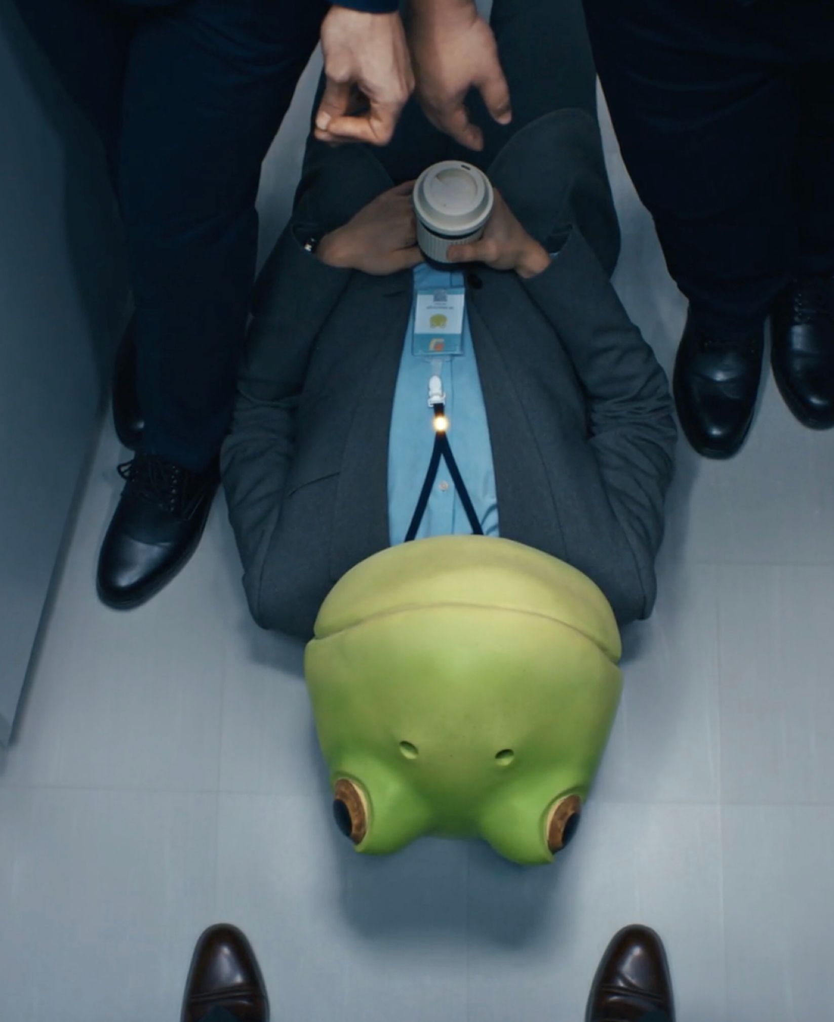 Office worker in a suit lying on the floor with a green frog mask, seen from above