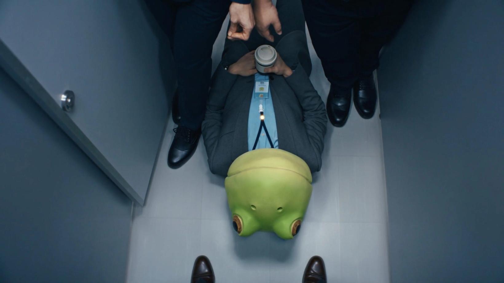 Office worker in a frog mask lying on the floor of a bathroom stall, seen from above