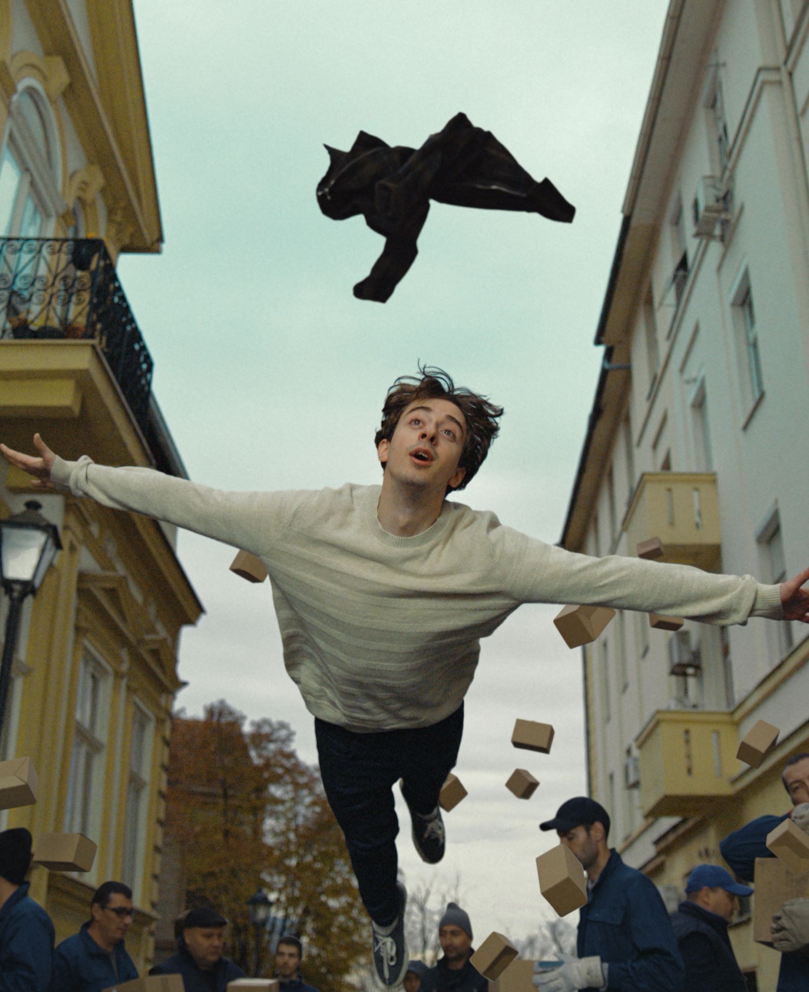 Man flying through a street with arms outstretched as movers and boxes scatter