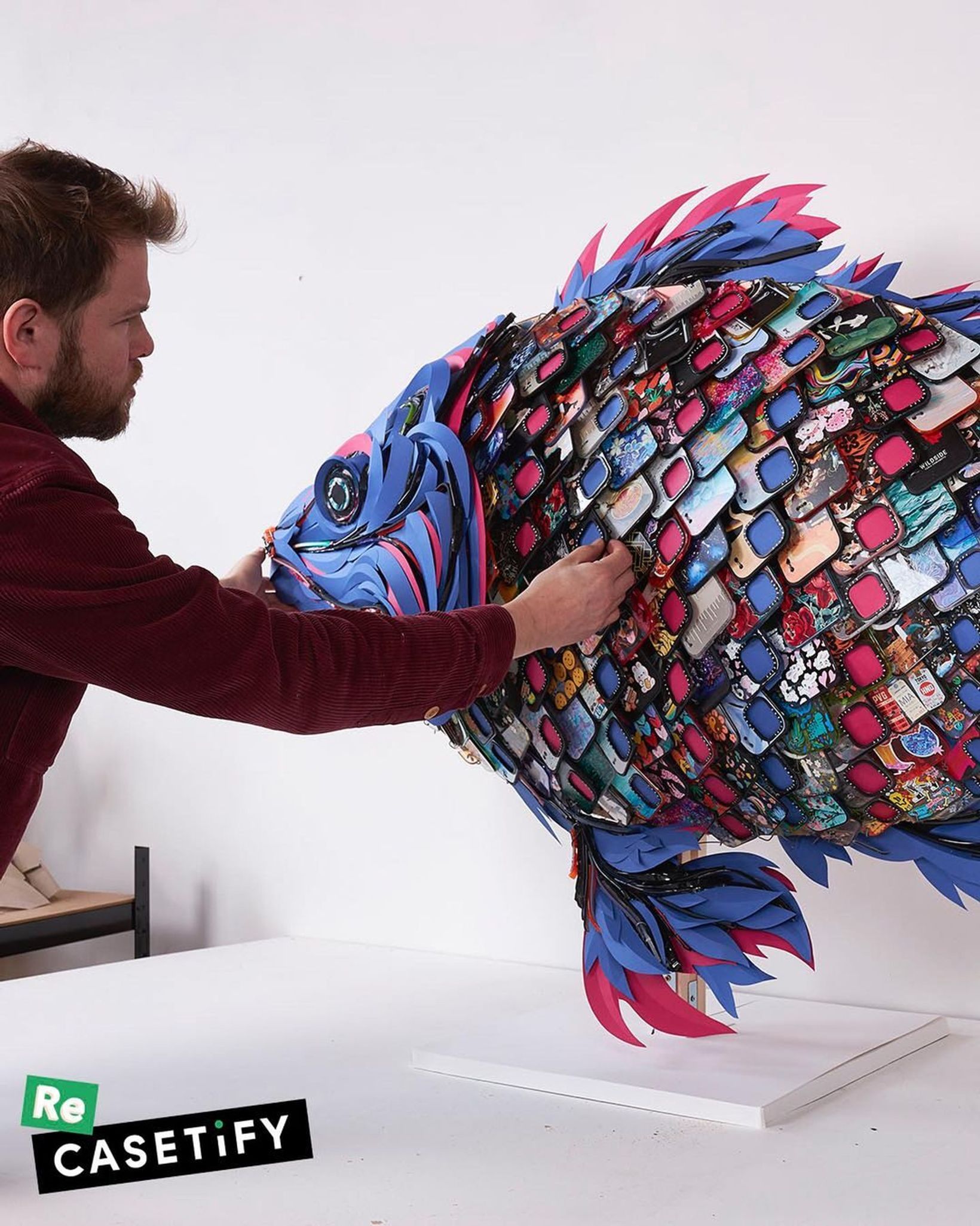 Artist placing phone case scales onto a large fish sculpture