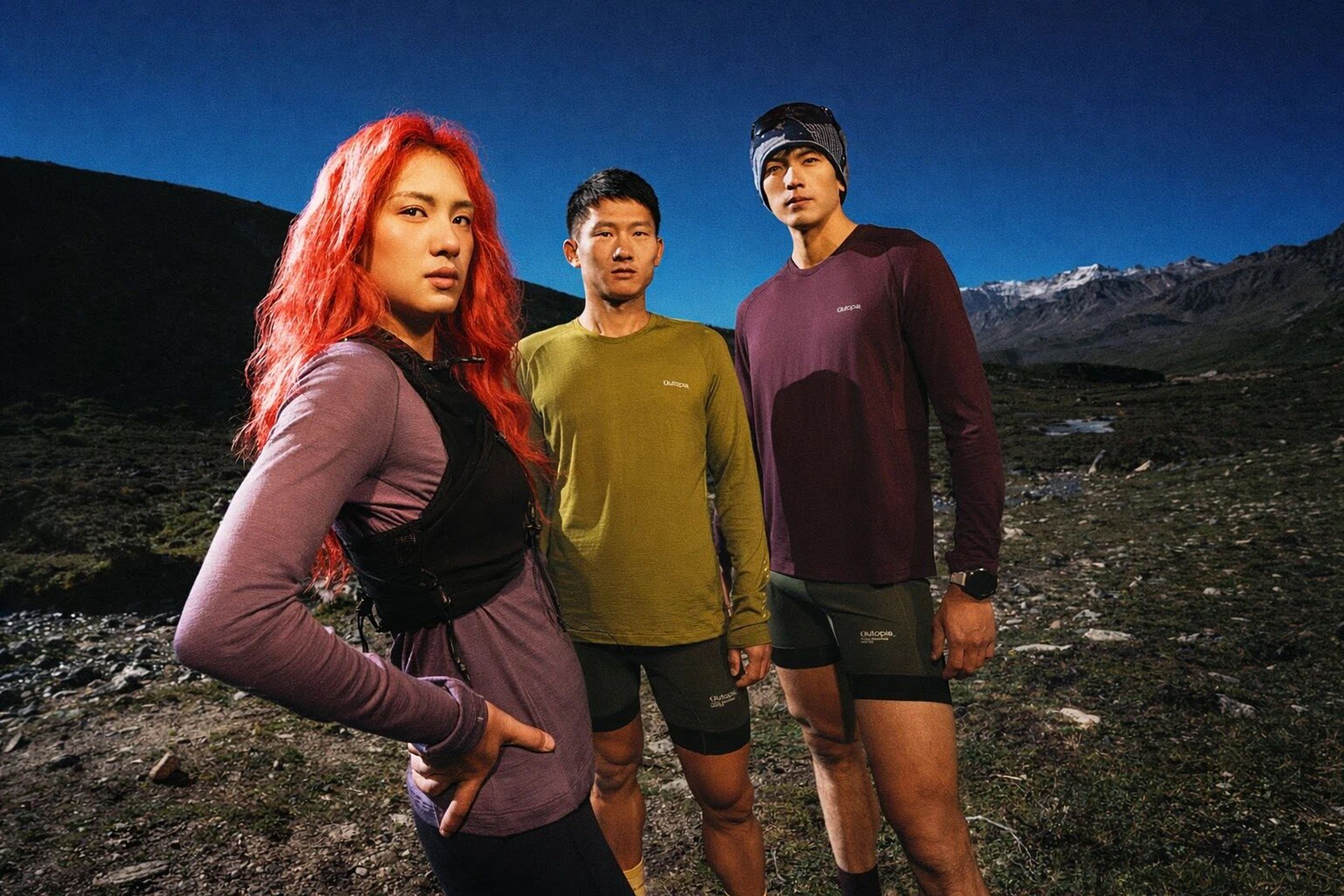Three trail runners in Outopia apparel standing on a mountain ridge at dusk