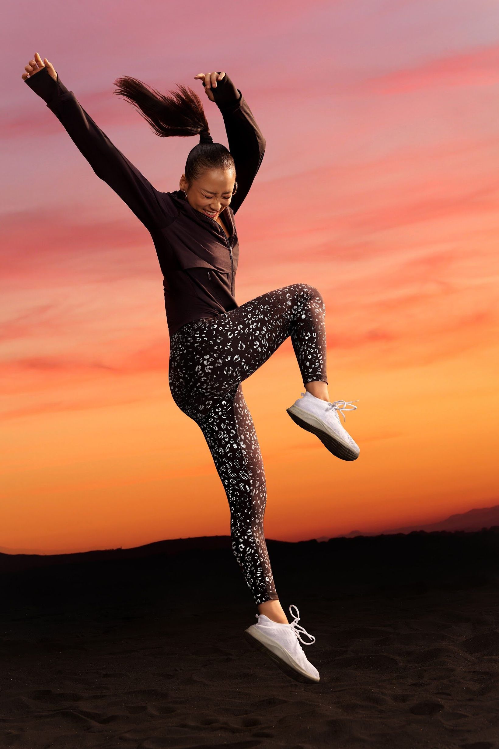 Woman jumping with arms raised in leopard-print leggings at sunset