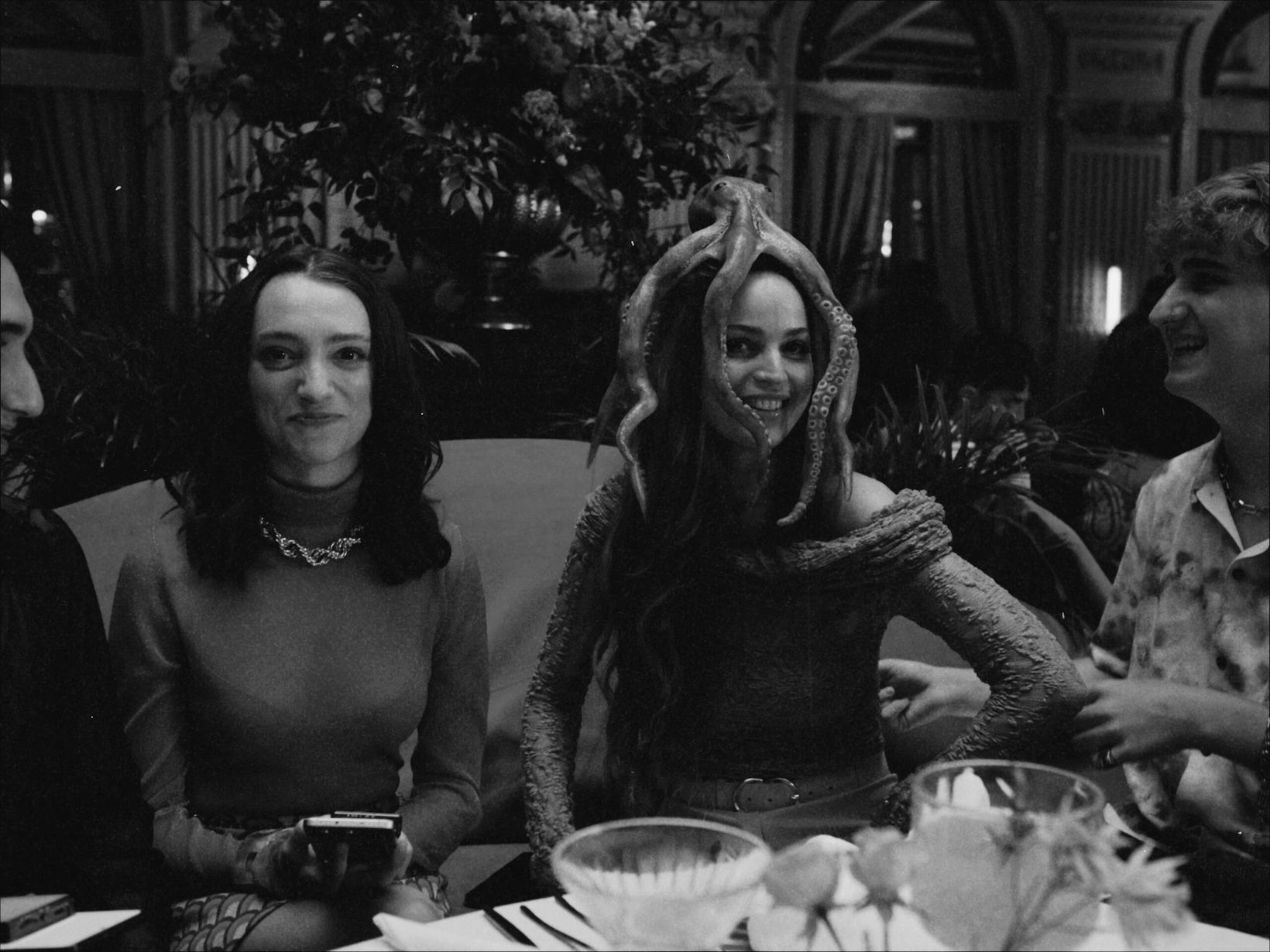 Black-and-white behind-the-scenes shot of cast seated at a dinner table