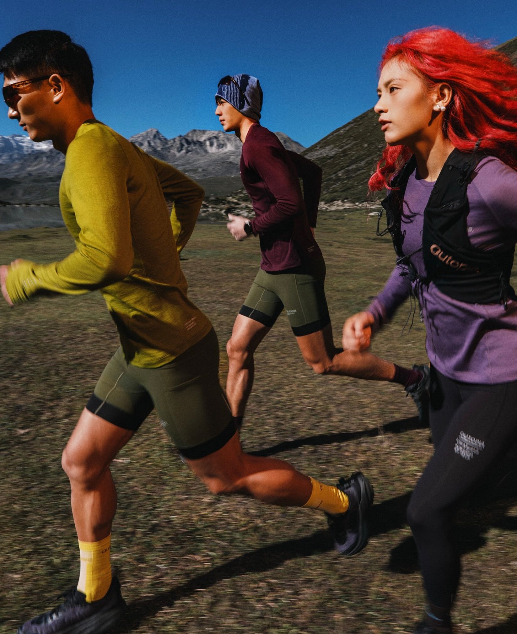 Three trail runners in Outopia apparel running across a mountain meadow