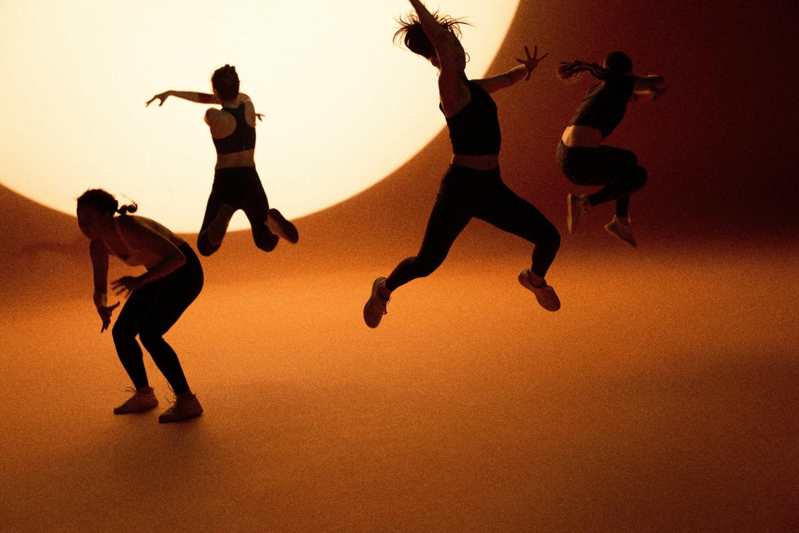 Silhouetted women jumping in front of a glowing sun on an orange set