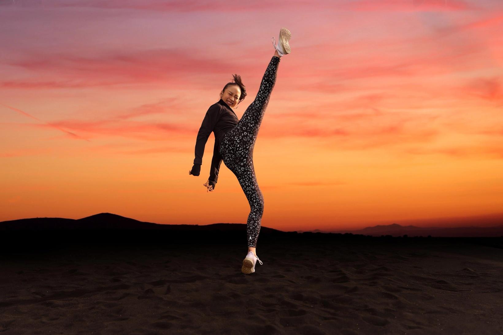 Woman kicking high against a pink and orange sunset