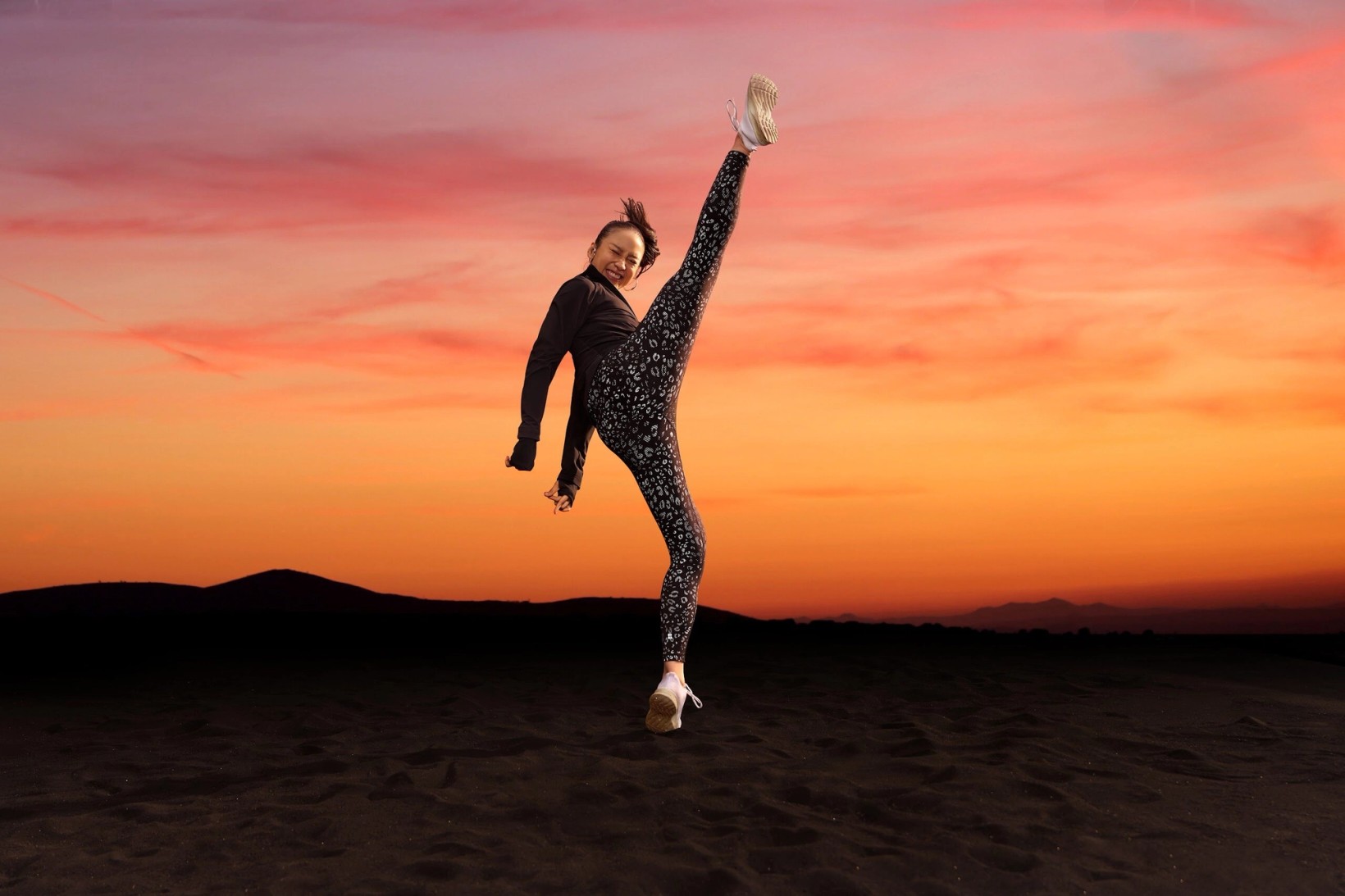Woman kicking high against a pink and orange sunset