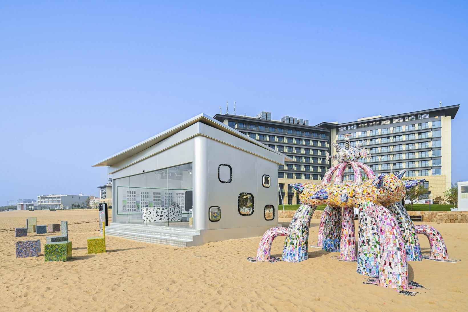 Silver exhibition pavilion and phone-case sculpture on the beach in Aranya
