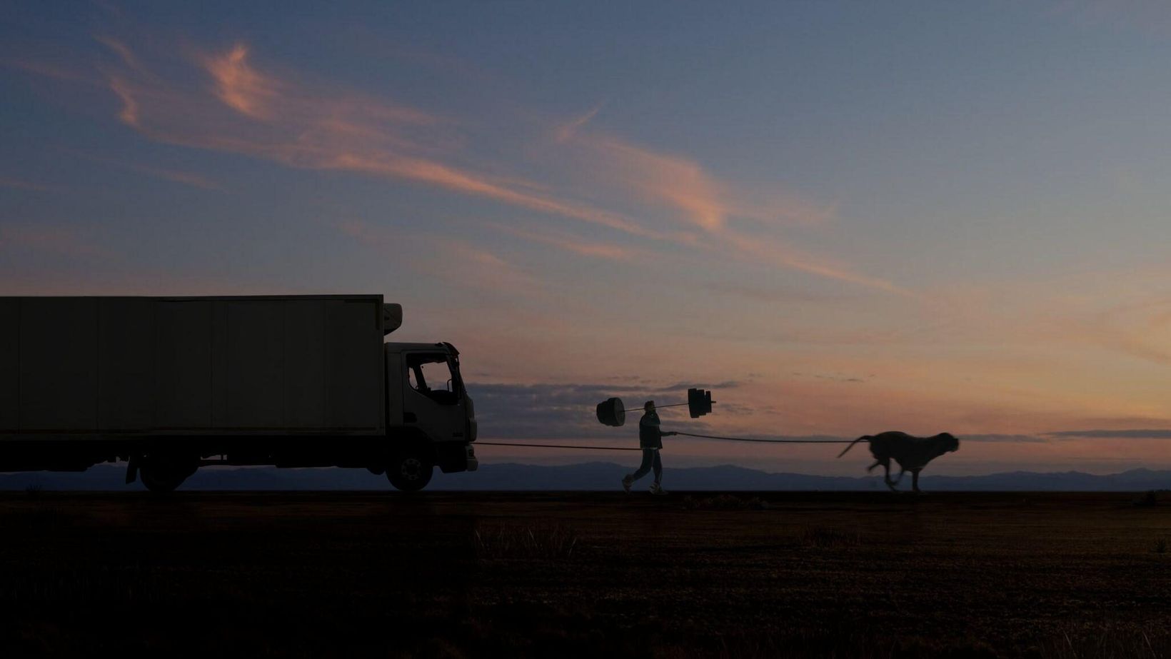Silhouettes of a truck, a runner and a dog against a sunset sky