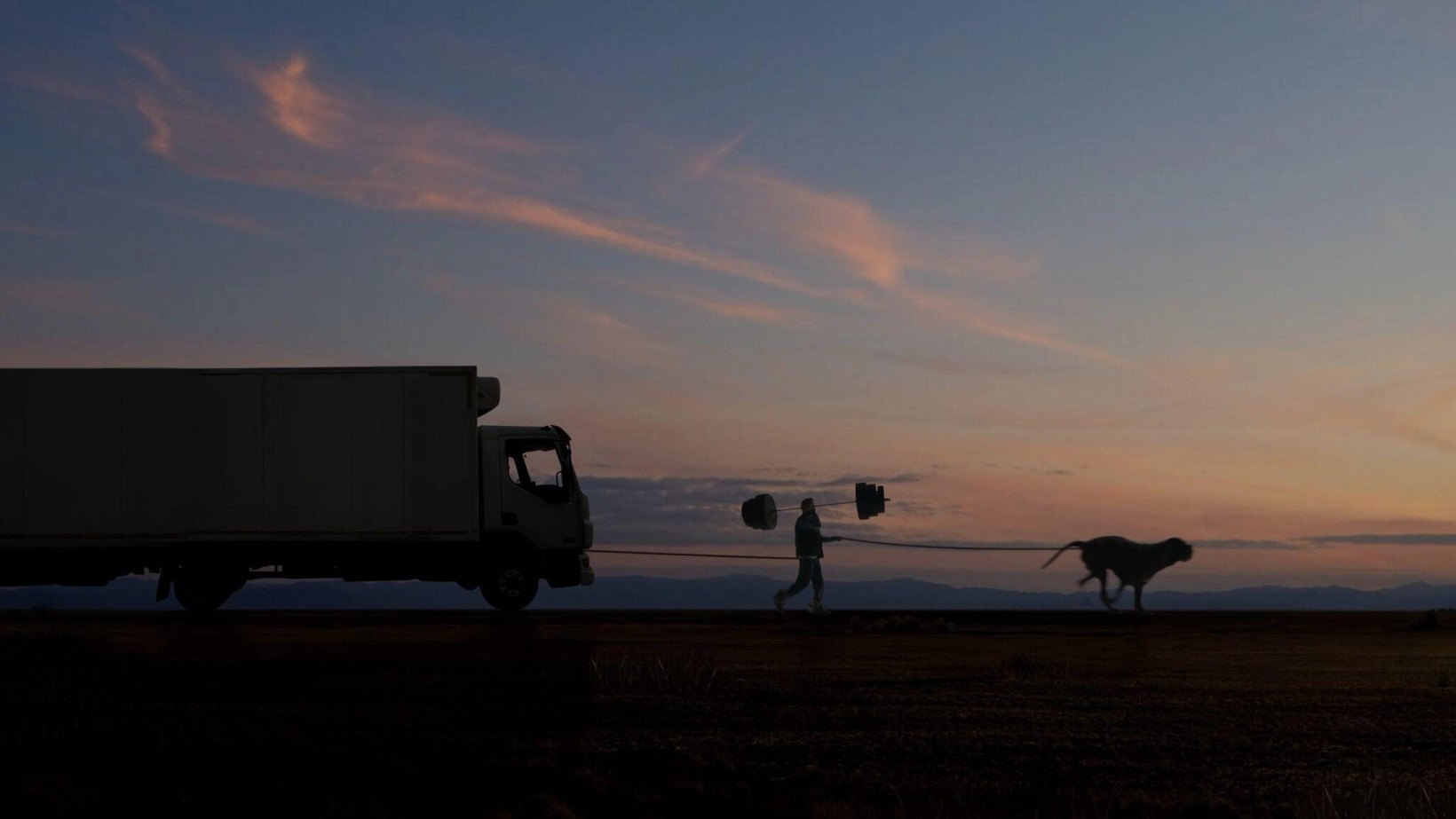 Silhouettes of a truck, a runner and a dog against a sunset sky