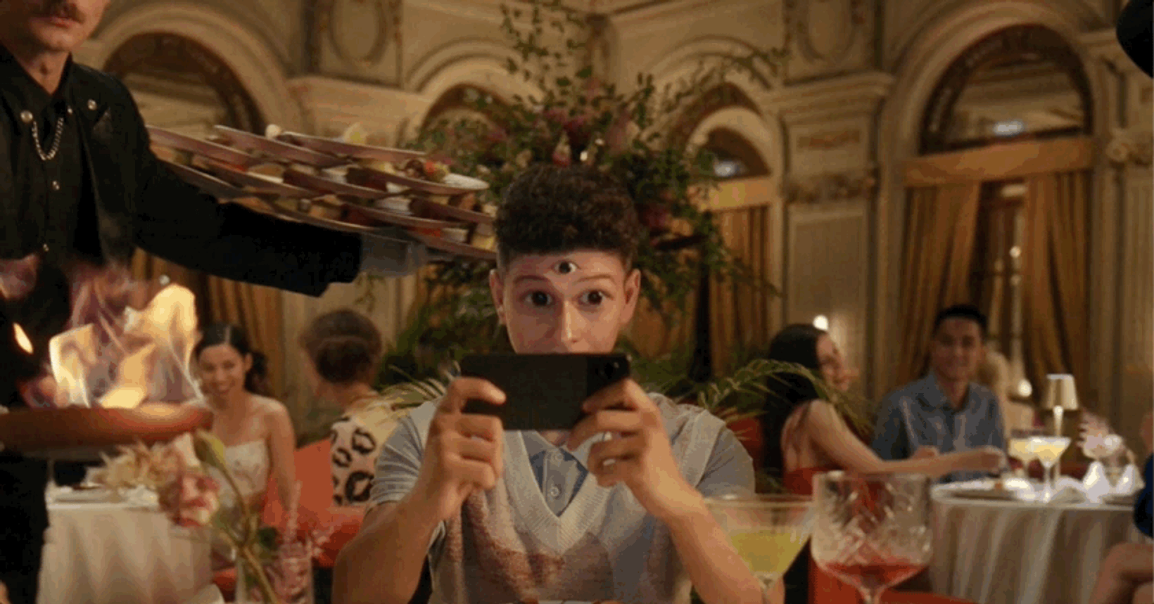Guest filming with a phone as waiters carry trays through the restaurant