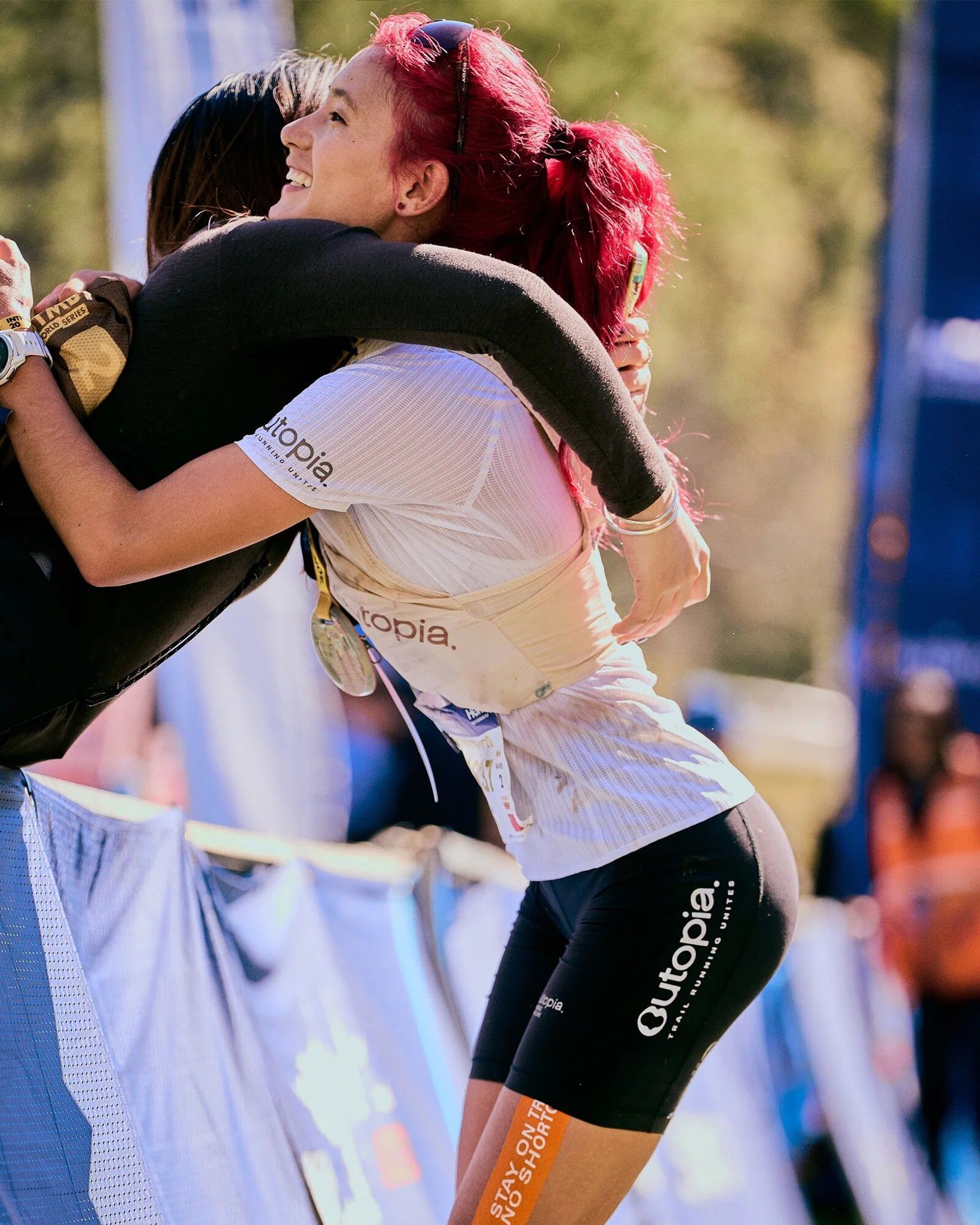 Two runners hugging at a finish line wearing Outopia race gear