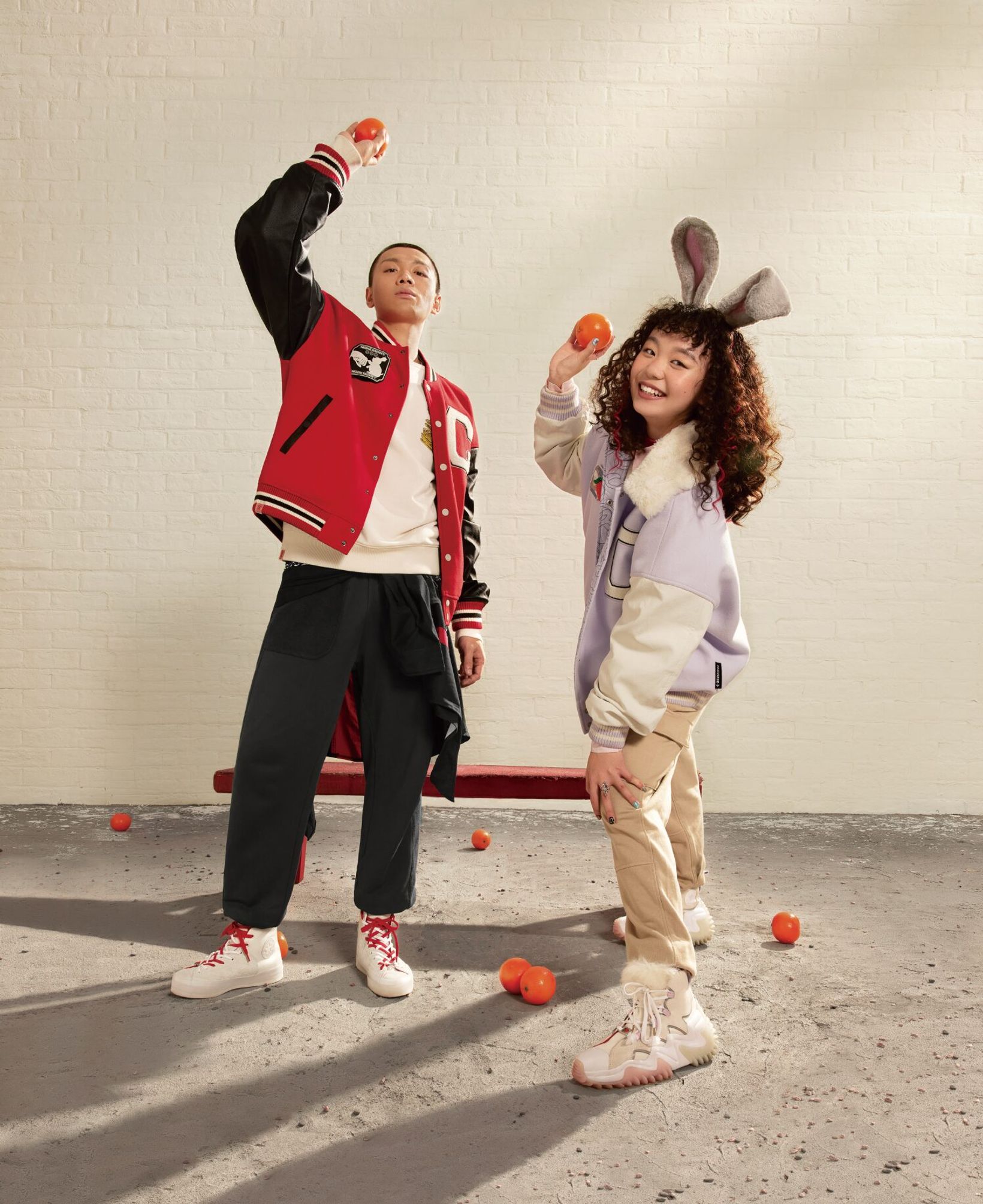 Two friends in bunny ears and Converse jackets dancing with carrots on the floor
