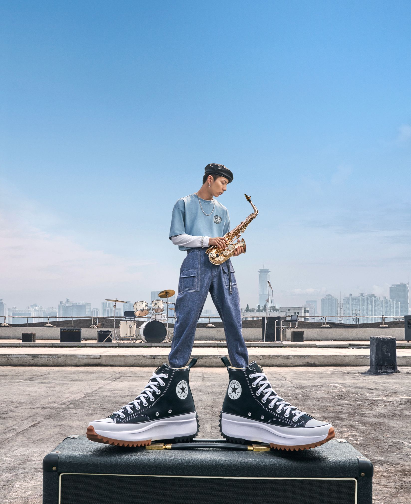 Saxophonist standing on an amp in Converse platform high-tops on a city rooftop