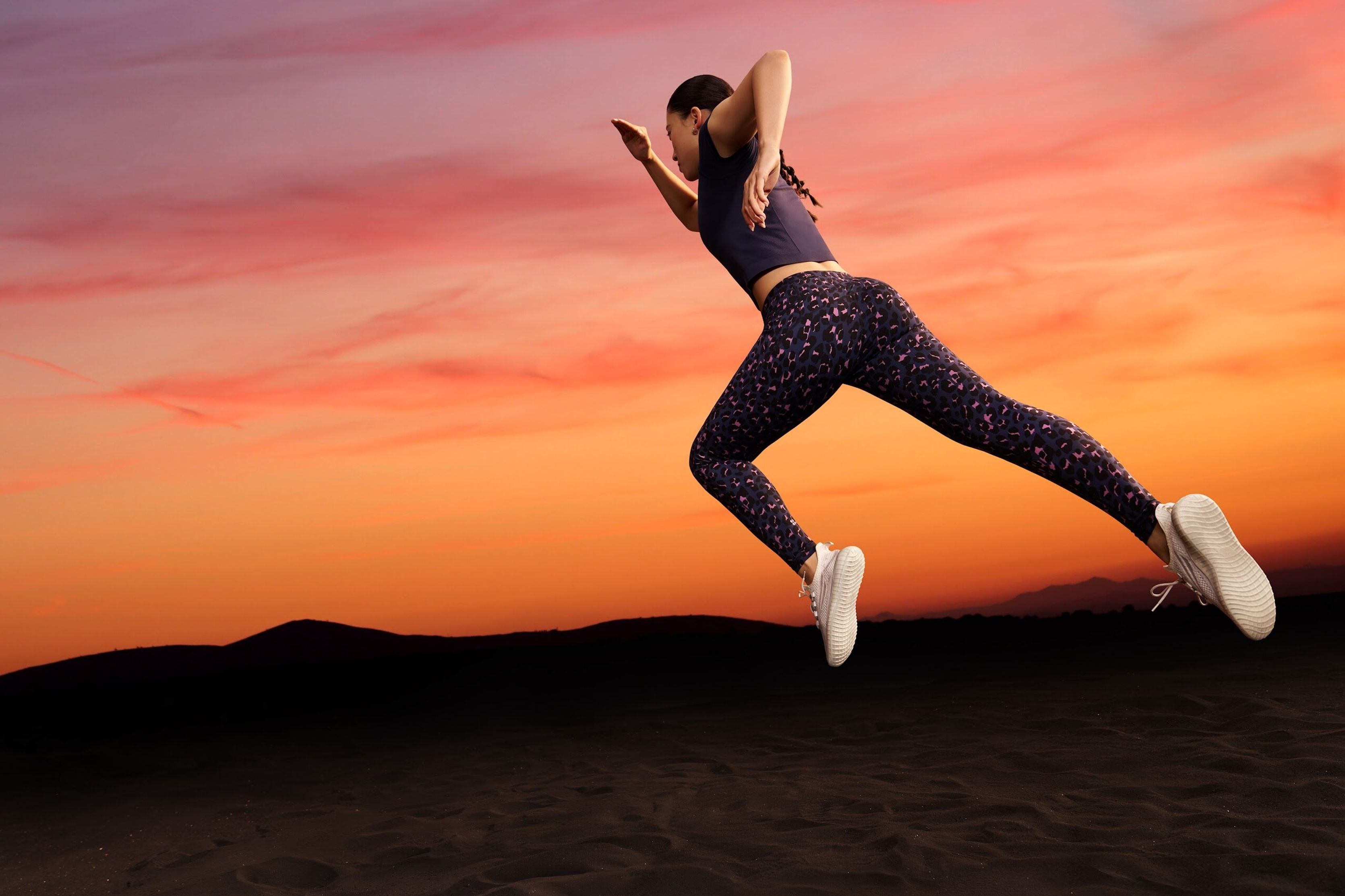 Woman leaping in Sweaty Betty leggings against an orange sunset