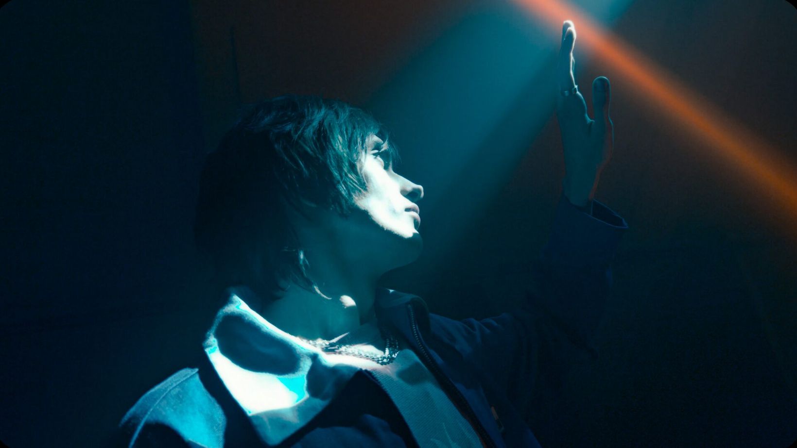 Film still of a woman looking up into a beam of teal light