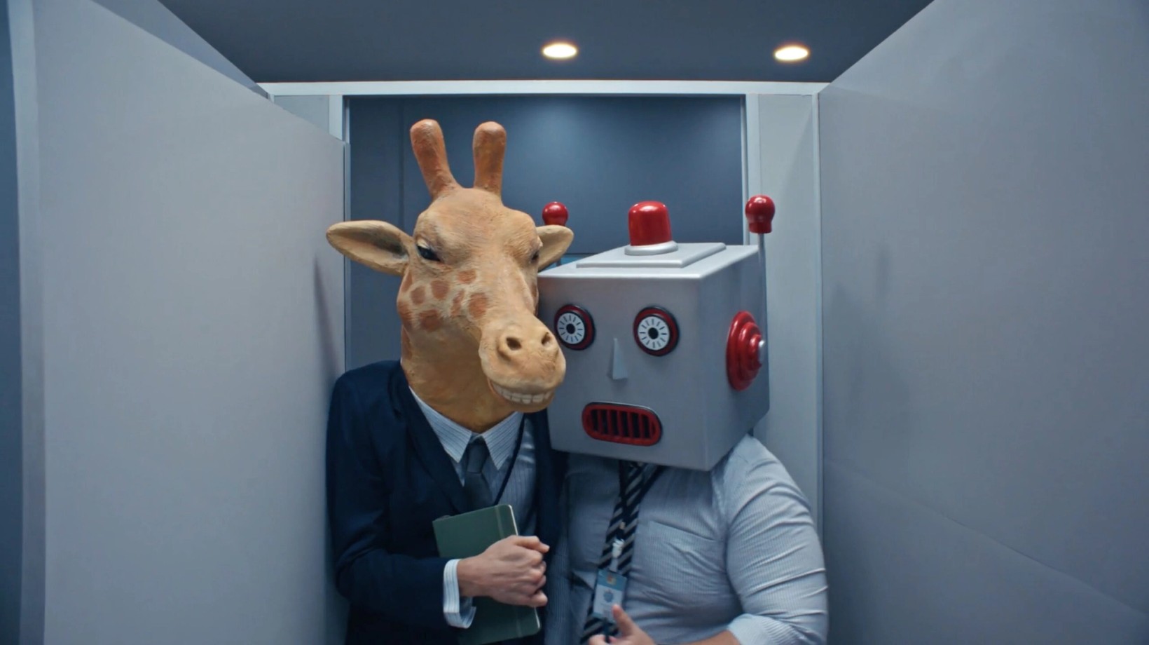 Two office workers in giraffe and robot masks squeezed into a bathroom stall