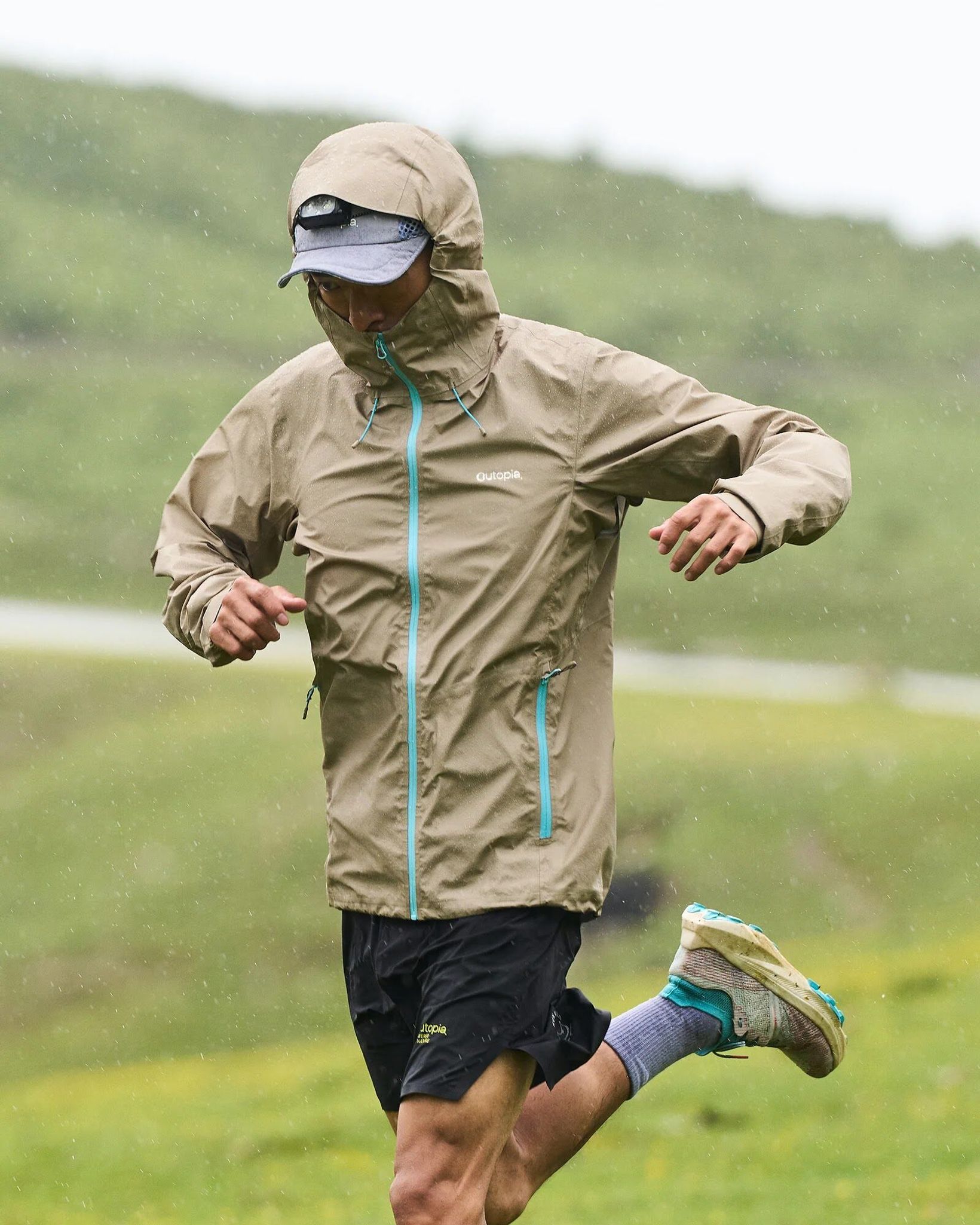 Runner in a beige Outopia jacket running on a grassy hillside