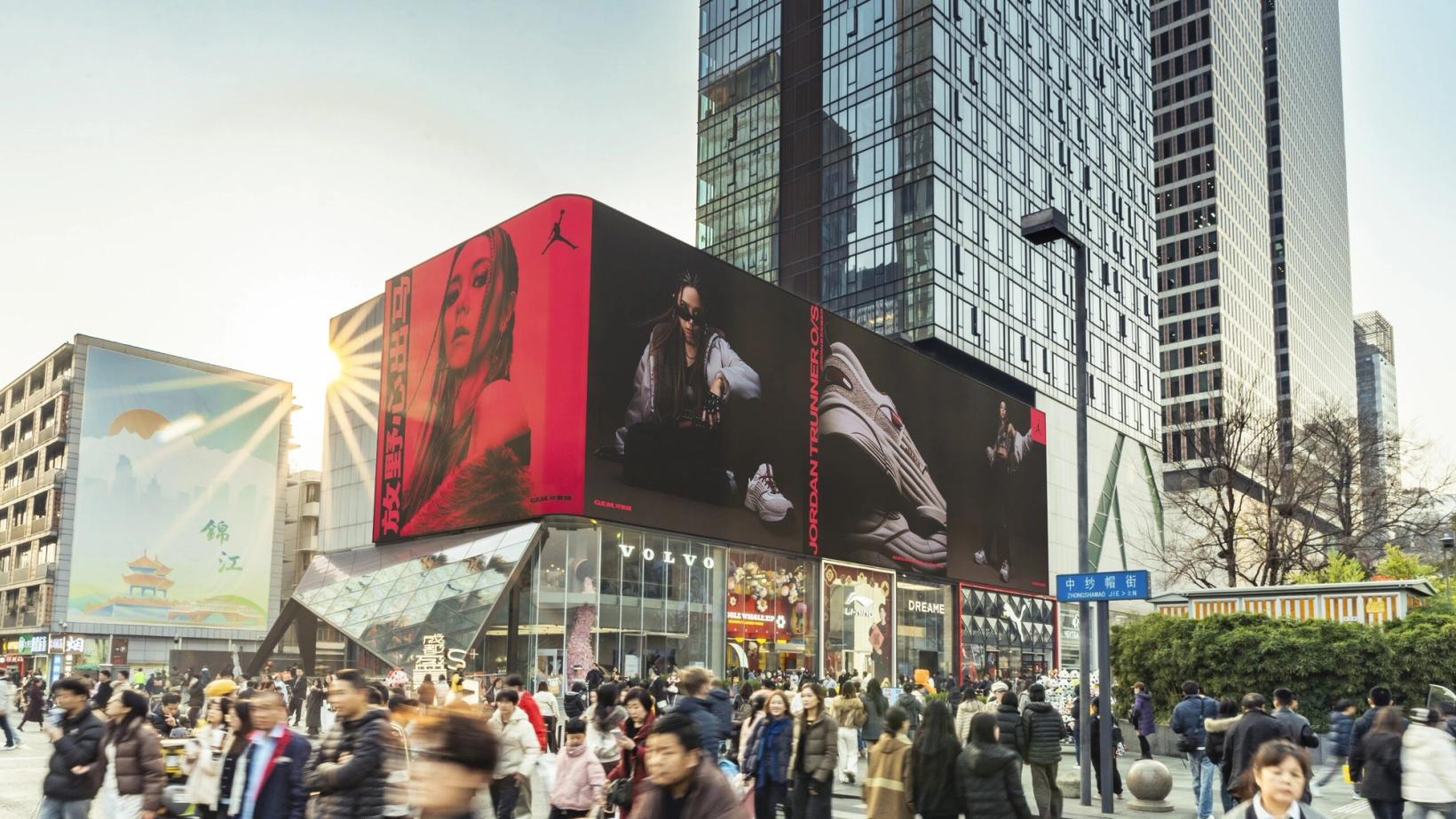 Curved outdoor screens showing the campaign above a crowded plaza